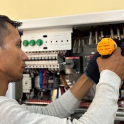 Skilled electrician using a drill to repair electrical equipment indoors. Focus on precision and safety.