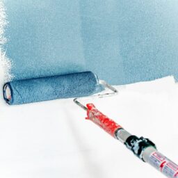 A paint roller applying blue paint to a white wall