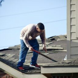 A person in a long-sleeved shirt removing shingles from a residential roof