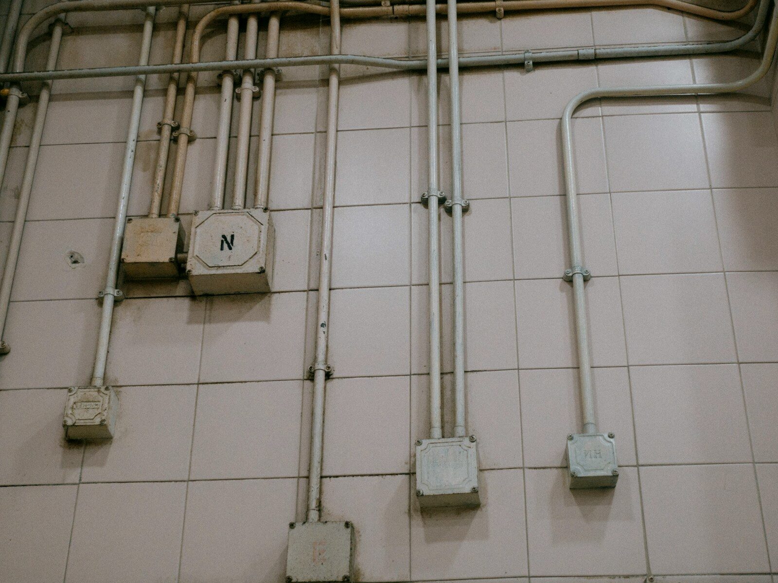 a tiled wall with pipes and a clock on it
